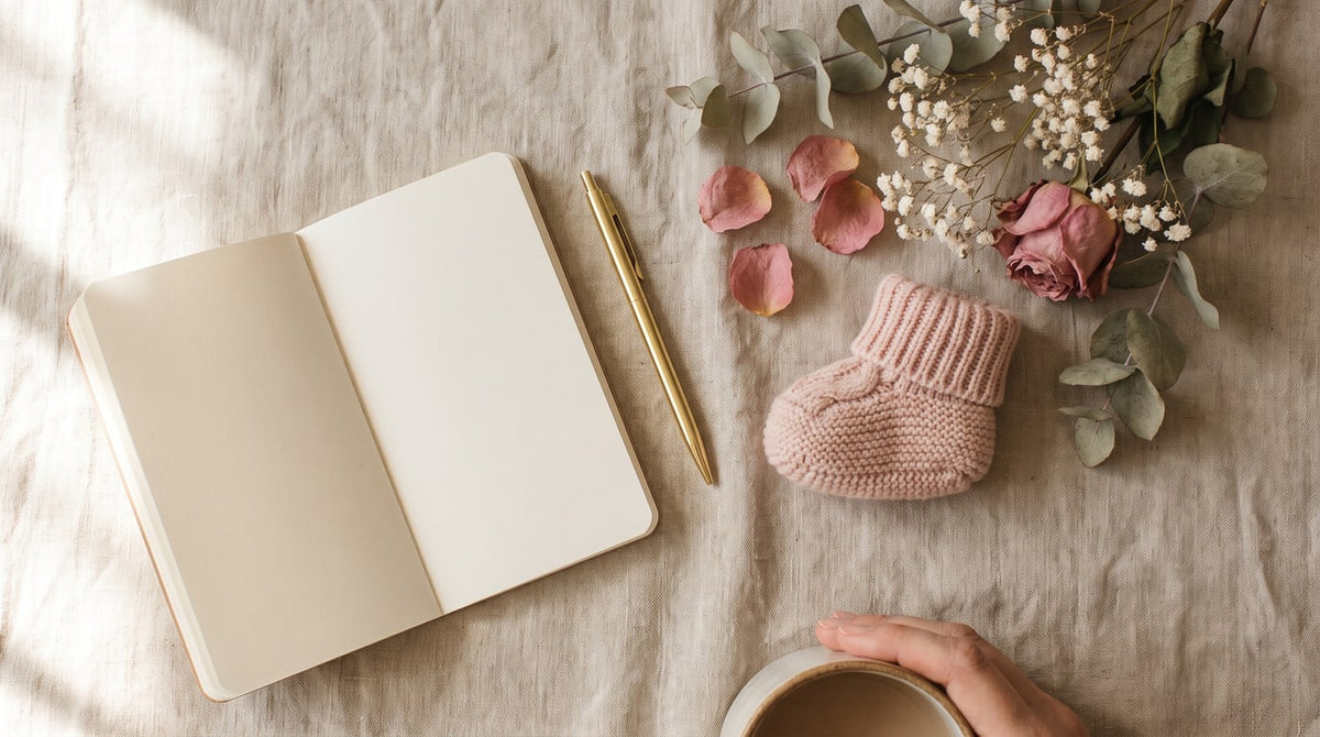 Leerer Wochenplaner, Goldstift, altrosa Babyschuh und getrocknete Blumen auf Leinen