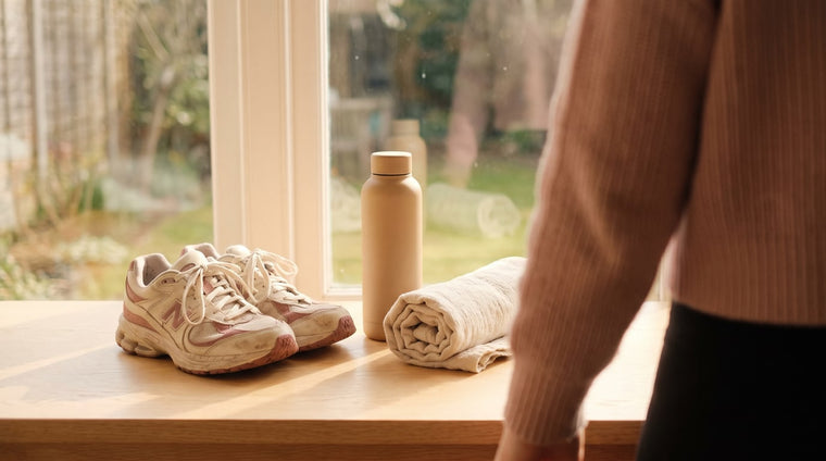 Laufschuhe, eine Wasserflasche und ein cremefarbenes Handtuch am hellen Fenster im warmen Tageslicht