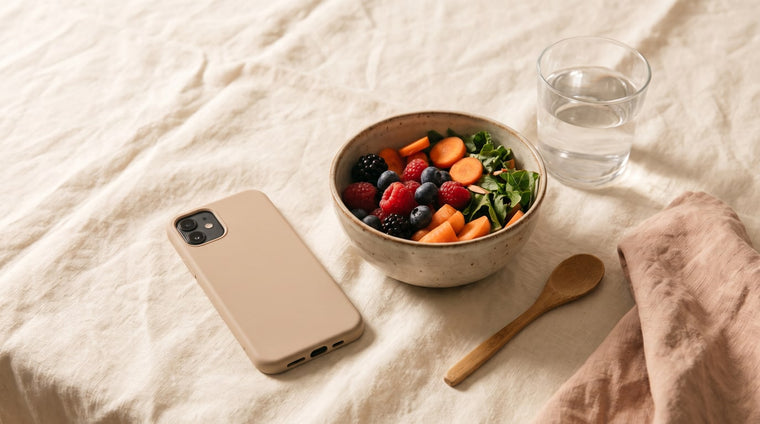 Smartphone mit dunklem Display neben einer Schale mit frischem Obst und Gemuese und einem Glas Wasser auf Leinen