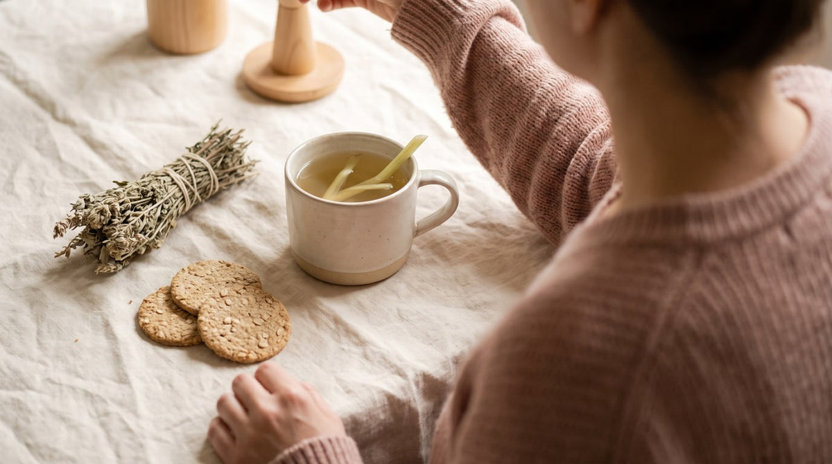 Tasse Fencheltee mit Crackern und getrockneten Kräutern auf cremefarbenem Leinen im warmen Licht