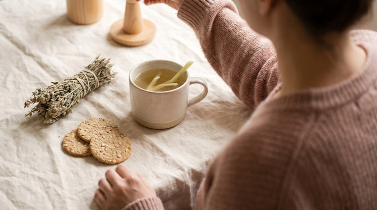 Tasse Fencheltee mit Crackern und getrockneten Kräutern auf cremefarbenem Leinen im warmen Licht
